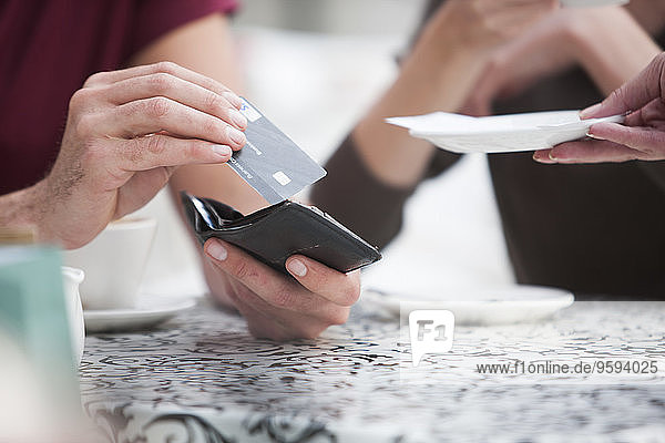 Mann bezahlt Rechnung mit Kreditkarte in einem Straßencafé