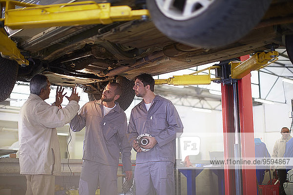Two car mechanics with client in repair garage