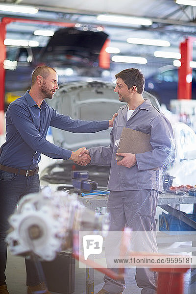 Car mechanic and client shaking hands in repair garage