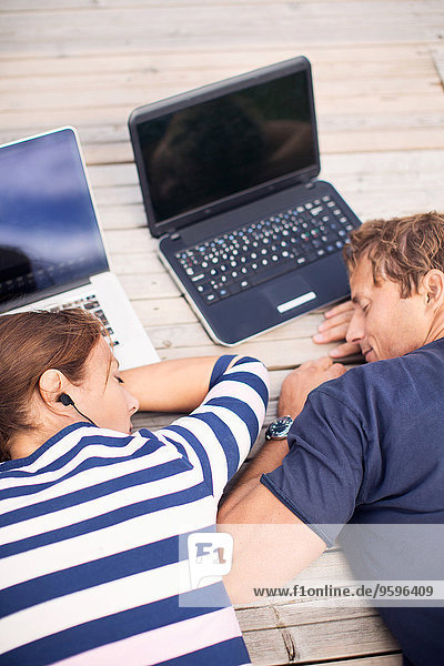 Hochwinkelansicht des reifen Paares mit Laptops am Pier