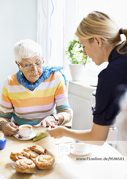 Female examining senior woman's finger at breakfast table in nursing home
