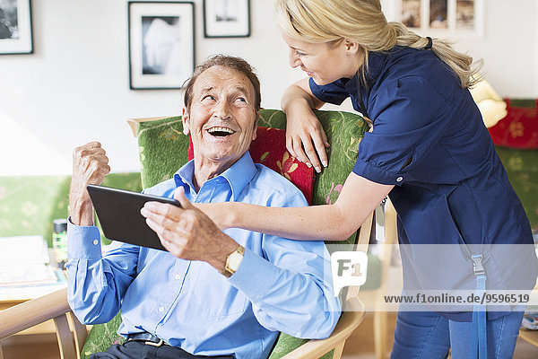Glückliche Senioren und Frauen mit digitalen Tabletts im Pflegeheim