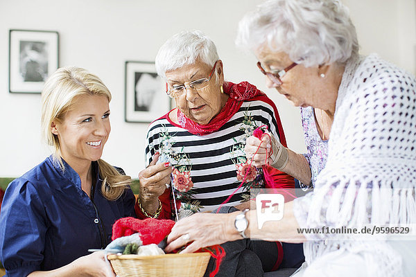 Eine glückliche Frau  die ältere Frauen beim Stricken im Pflegeheim beobachtet.