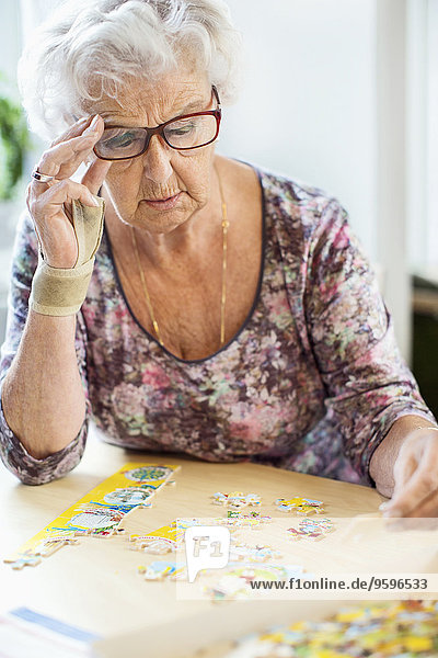 Seniorenfrau löst Puzzle am Tisch im Pflegeheim