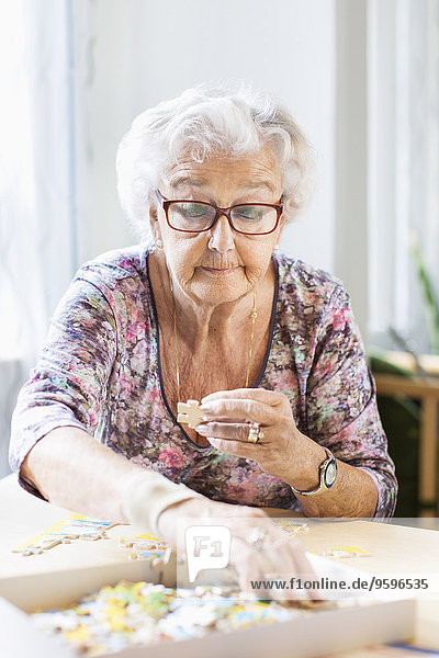 Seniorin beim Zusammenbau von Puzzleteilen am Tisch im Pflegeheim