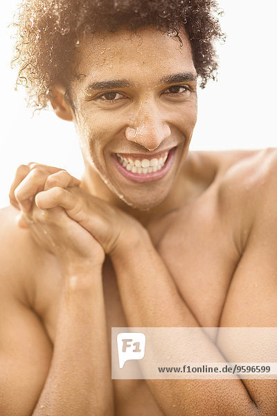 Porträt eines fröhlichen nassen Mannes ohne Hemd mit im Freien gefesselten Händen