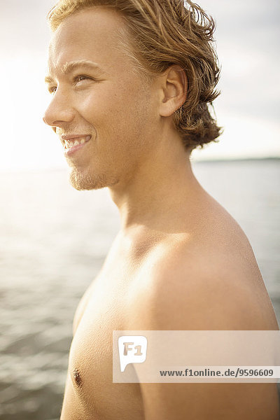 Seitenansicht eines glücklichen Mannes ohne Hemd  der am See wegschaut