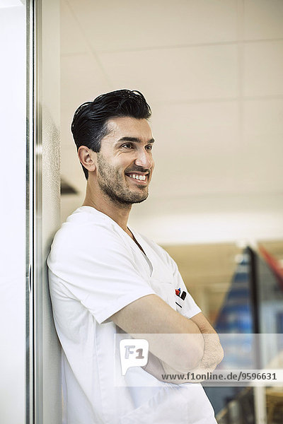 Smiling young male doctor leaning on wall in hospital