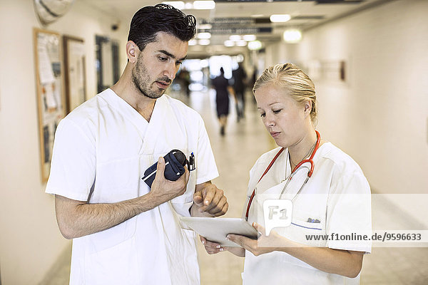 Male and female doctors discussing over digital tablet in hospital corridor