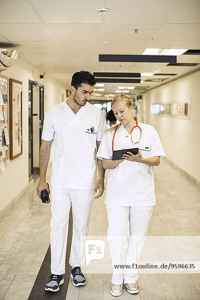 Full length of doctors discussing over digital tablet in hospital corridor
