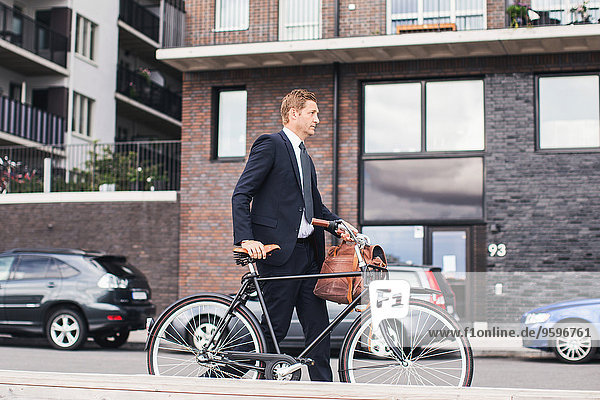 Businessman walking on city street with bicycle against buildings