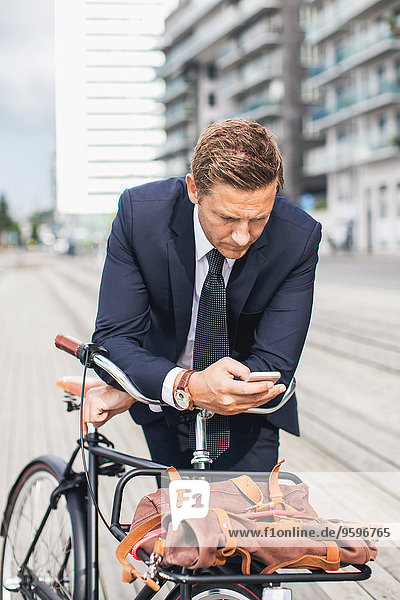Geschäftsmann mit Smartphone in der Stadt beim Fahrradfahren