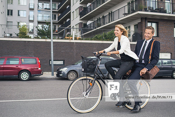 Happy business people riding on bicycle in city street