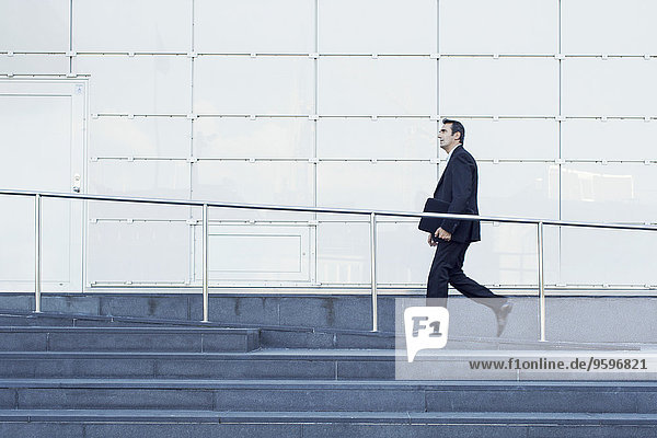 Seitenansicht eines Geschäftsmannes  der an einem Geländer vor dem Bürogebäude entlanggeht.