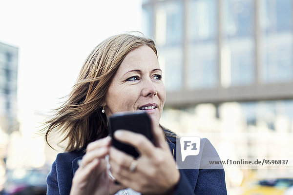 Businesswoman looking away while using mobile phone outdoors