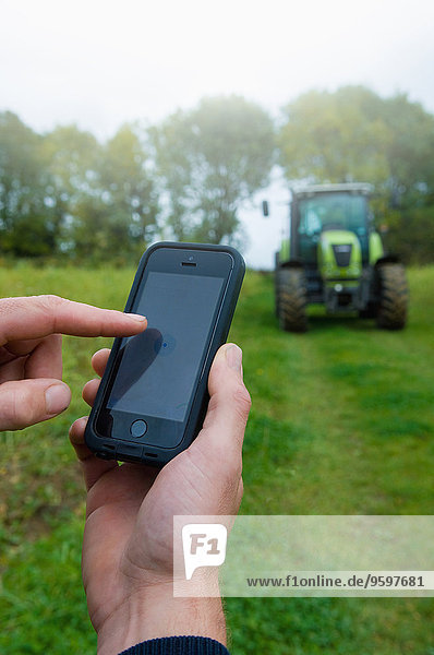 Nahaufnahme der Hand des Landwirts über Touchscreen am Smartphone im Feld