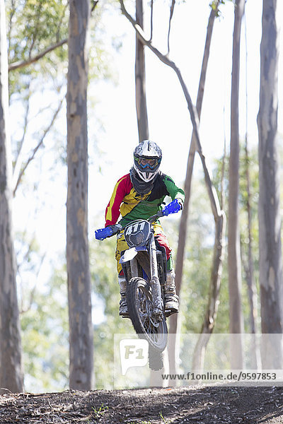 Junger männlicher Motocross-Fahrer beim Springen in der Luft im Wald