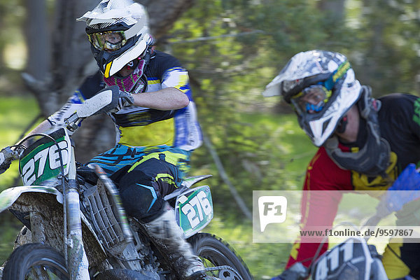 Zwei junge männliche Motocross-Fahrer rasen durch den Wald
