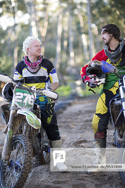 Two young male motocross competitors chatting on forest track