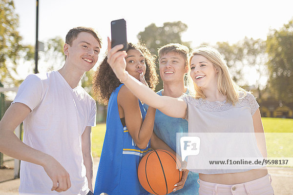 Four young adult basketball players taking smartphone selfie