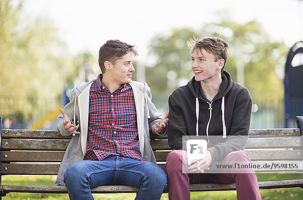 Zwei junge männliche Freunde beim Plaudern auf der Parkbank