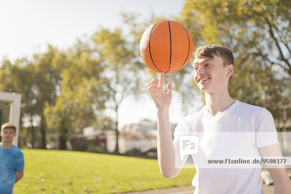 Lächelnder junger Basketballspieler  der Basketball auf dem Finger balanciert.