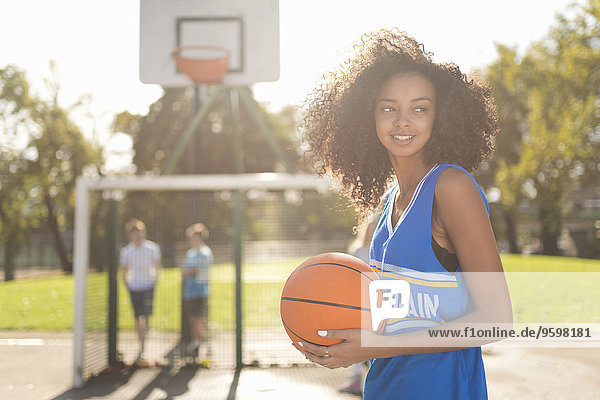 Lächelnde junge Basketballspielerin hält Basketball