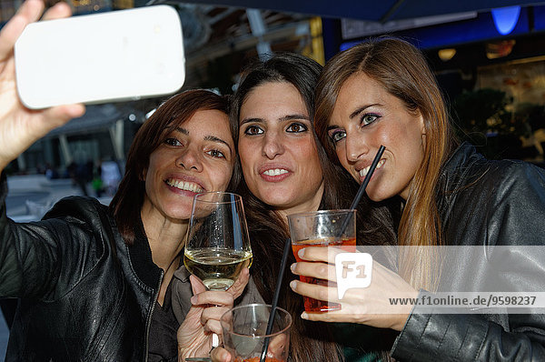 Drei Freundinnen in der Bar  die sich mit dem Smartphone selbst porträtieren.