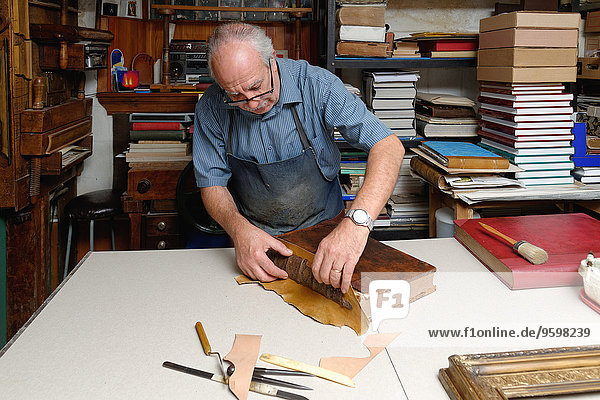 Senior Mann repariert antiken Buchrücken in traditioneller Buchbinderei