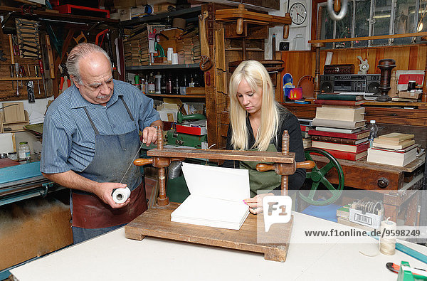Senior man and young woman preparing to bind pages with thread in traditional bookbinding workshop