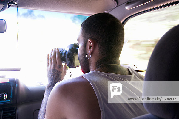 Young man taking photographs through car windscreen