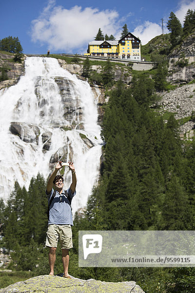Junger Mann nimmt Smartphone Selfie vor Toce Wasserfall  Formazza  Verbania  Piemonte  Italien