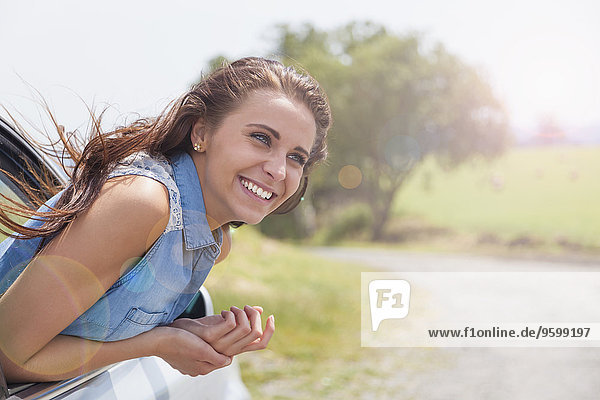 Young woman leaning out of car window on road trip