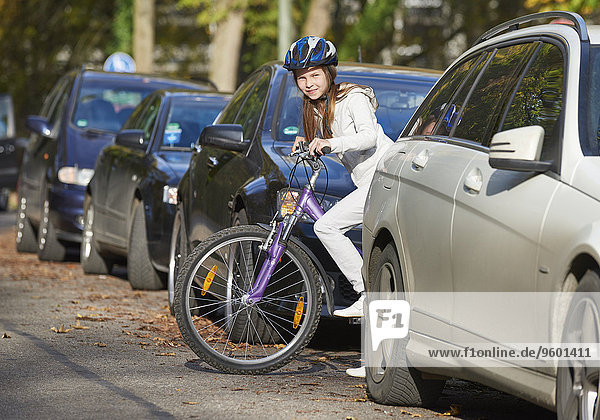 Mädchen steht mit Fahrrad zwischen parkenden Fahrzeugen
