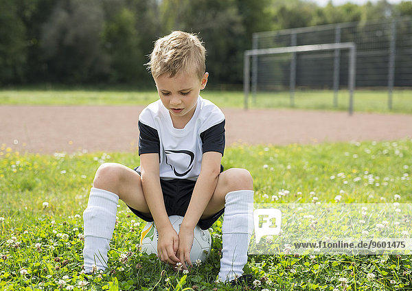 Kleiner Junge auf Sportplatz  sitzt auf Fußball