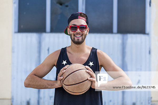 Portrait of smiling young man with basketball wearing basecap and sunglasses