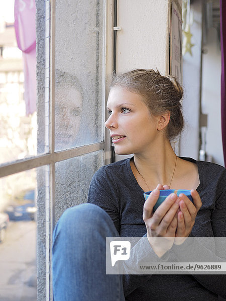 Junge Frau mit Teebogen durchs Fenster schauend