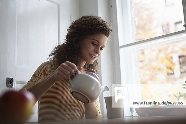 Junge Frau gießt Tee in die Tasse