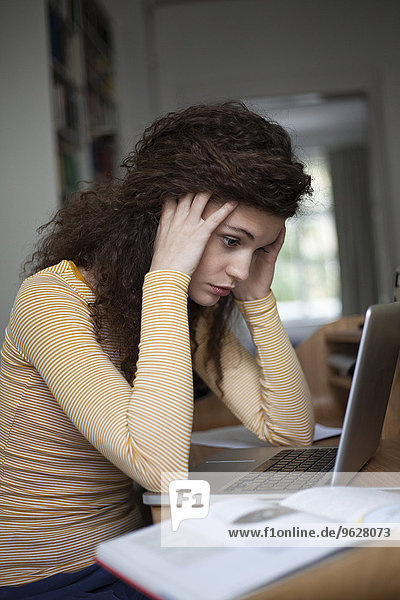 Überlastete junge Frau mit Laptop im Home Office