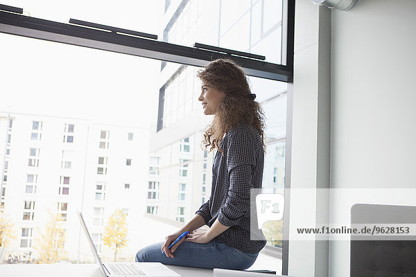 Young woman at desk in office looking out of window