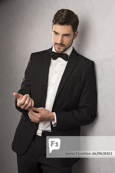 Portrait of man wearing dinner jacket and bow leaning at wall