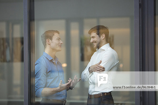 Two businessmen communicating behind window in an office