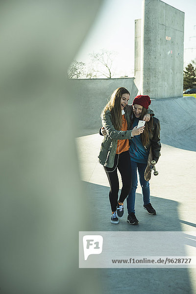 Zwei glückliche Teenagerinnen mit Handy im Skatepark
