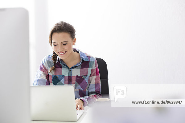 Lächelnde junge Frau mit Laptop am Schreibtisch