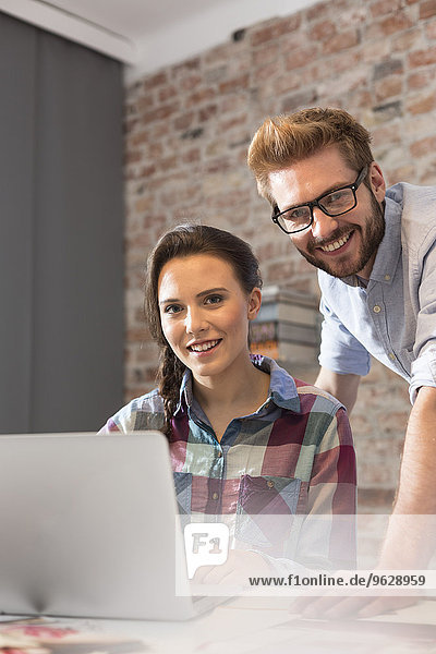 Smiling young woman and man with laptop in office