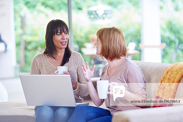 Zwei Frauen sitzen auf der Couch mit Laptop und Tassen