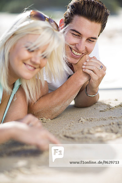 Young couple lying on the beach and drawing in the sand