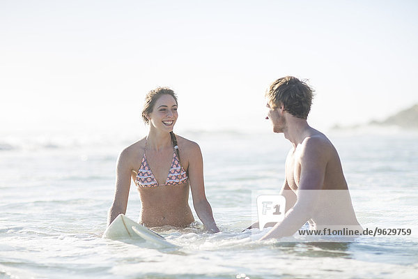 Glückliches junges Paar mit Surfbrett im Meer