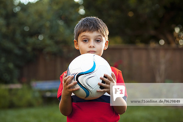 Junge hält Fußball gegen Brust im Garten