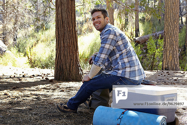 Young man in forest sitting on cool box  Los Angeles  California  USA